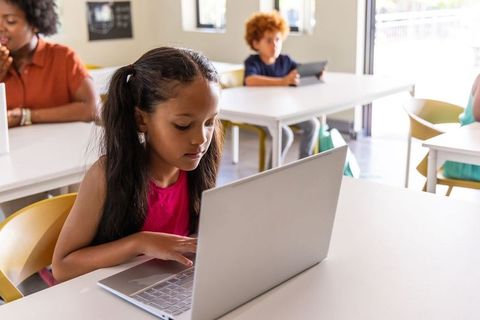 Students using laptops and tablets in sunlit elementary classroom for digital learning