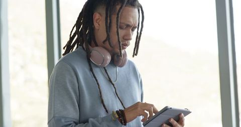 African american man tapping tablet with headphones, modern workspace, productivity, focus