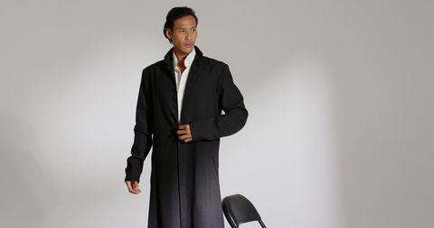 Stylish man in long black coat looking confident in minimalist studio