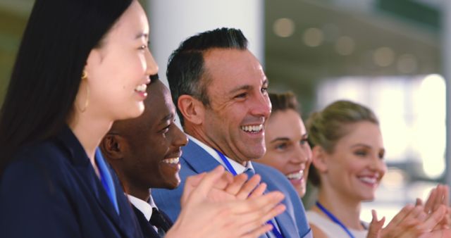 A diverse group of business professionals is seen clapping and smiling together, showcasing unity and collaboration within a corporate setting. This image can be used for themes related to teamwork, employee satisfaction, business success, corporate events, and multicultural workplace environments. Ideal for presentations, business blogs, and company websites to promote positive work culture and diversity.