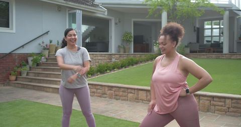 Diverse women exercising with smartwatches on manicured lawn outside modern house