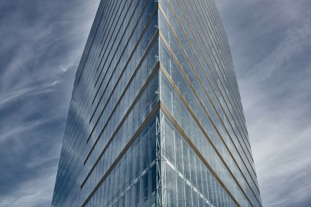Modern glass skyscraper towering against a dramatic sky, reflecting contemporary architecture and urban development. Suitable for use in corporate design, real estate presentations, architectural portfolios, and business-themed projects.