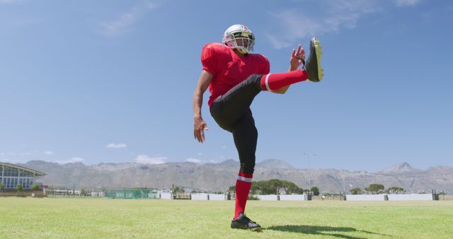 Biracial male american footballer kicking ball during training at sunny sports field, copy space. Sport, team sport, sports equipment and competition, unaltered.