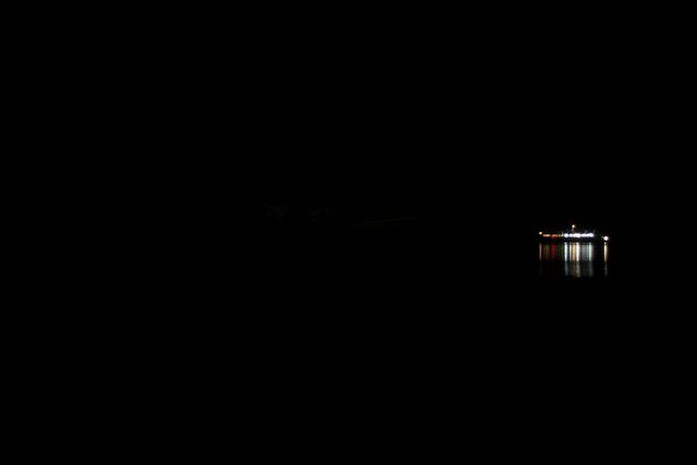 Solitary ship illuminated by bright lights on a dark and calm water. Ideal for themes of isolation, solitude, maritime, night-time ambiance, and peaceful travel. Useful for backgrounds, travel articles, and promotional materials focusing on night travel or sea journeys.