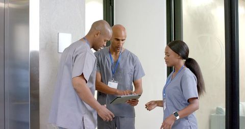 Three African American clinicians collaborating over tablet in modern clinic corridor