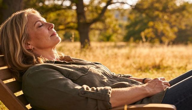 Mature woman relaxing on meadow bench, basking in warm golden hour sunlight