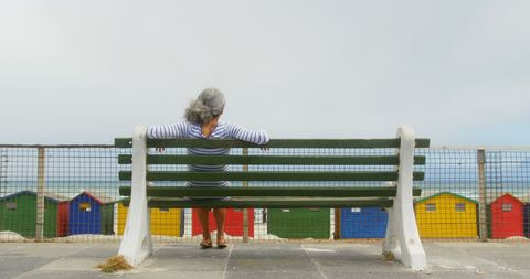 Senior Woman Relaxing on Bench Overlooking Colorful Beach Huts - Download Free Stock Images Pikwizard.com