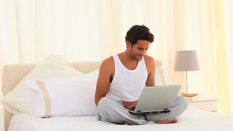 Man Relaxing on Bed Using Laptop in Bright Room