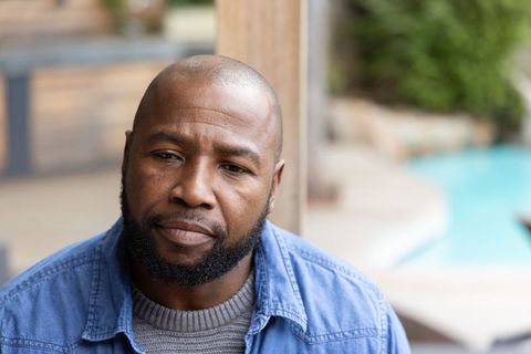 Contemplative african american middle-aged man sitting on patio beside pool in denim