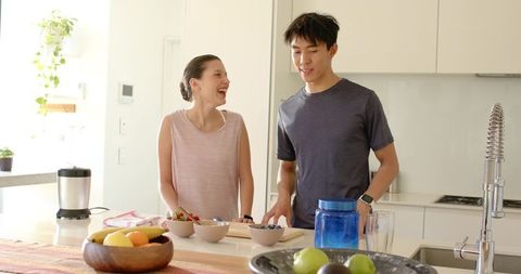 Young diverse couple chopping fruit and laughing at modern sunlit kitchen island