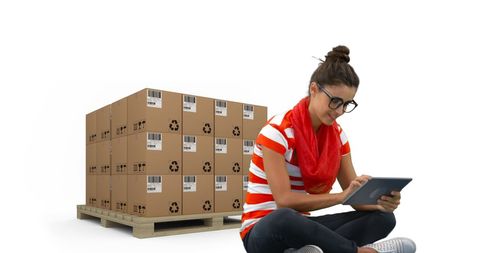 Woman using tablet with stacked shipping boxes indoors