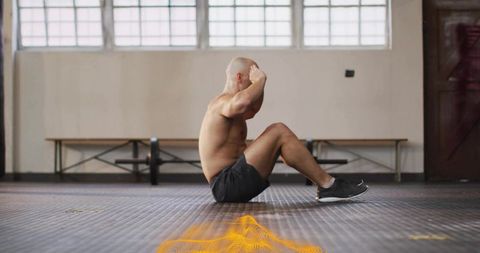 Shirtless athlete doing sit-up on rubber gym floor with barbell and orange overlay