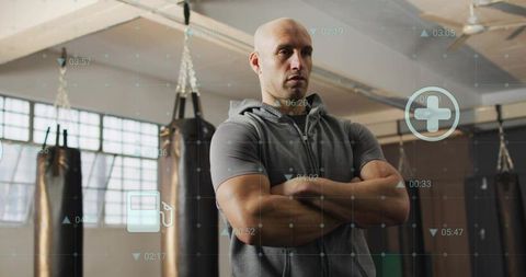 Bald trainer standing with arms crossed in industrial boxing gym with hud overlay