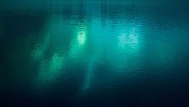 Turquoise night water reflection showing vertical teal light bands and gentle ripples