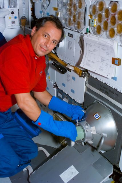 Astronaut on board the Space Shuttle Columbia is shown handling Biological Research in Canisters (BRIC) in GN2 freezer on the mid deck. This image can be used in articles and educational materials related to space exploration, scientific research conducted in space, or Michel Tognini's contributions to space missions representing France’s CNES. It illustrates astronaut involvement in maintaining and handling scientific experiments in a zero-gravity environment.