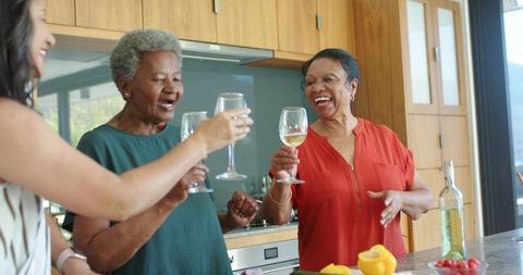 Senior african american women toasting wine at kitchen island celebrating friendship and joy