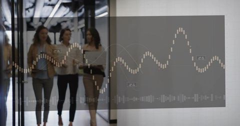 Three businesswomen walking and analyzing digital analytics overlay in modern glass office corridor