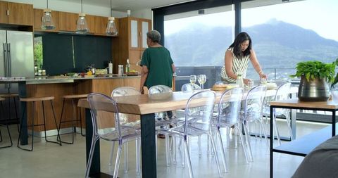 African american women preparing meal and arranging table in modern sunlit kitchen with view