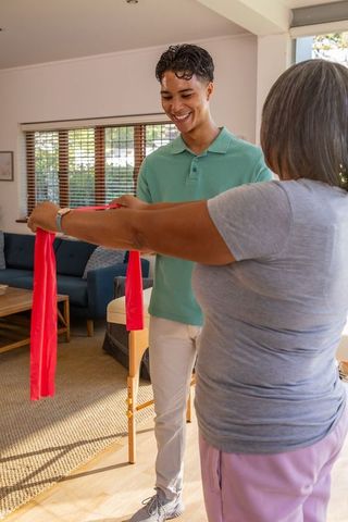 Hispanic trainer guiding senior woman using resistance band at home