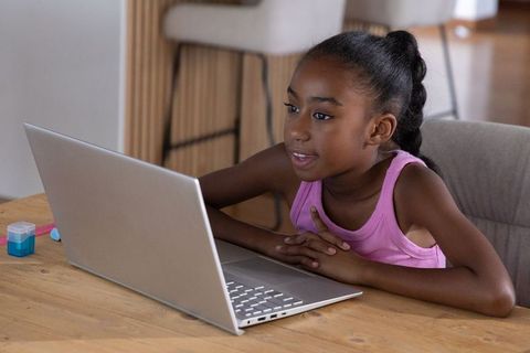 African american girl studying on laptop at home kitchen table remote learning