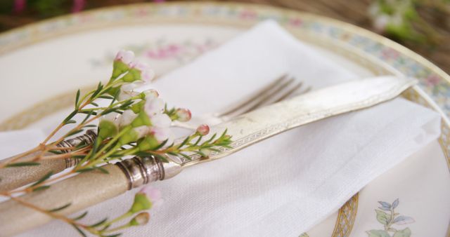 Vintage silverware is elegantly placed on a white napkin, adorned with delicate flowers, with copy space. It evokes a sense of sophistication and attention to detail, ideal for a formal dining setting or a special occasion.