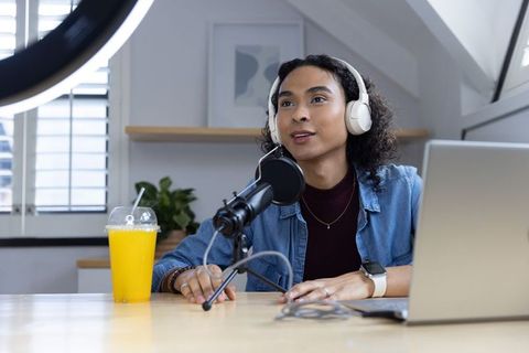 Non-binary creator recording podcast in bright home studio with headset, mic and laptop