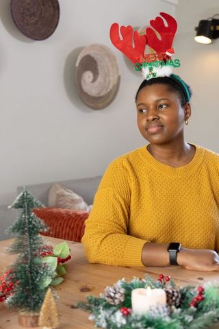 African american woman wearing reindeer antlers holding holiday wreath at cozy table