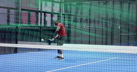 Male athlete swinging paddle on blue indoor court with neon glass reflections and led glow