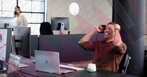 Young professional stretching at desk celebrating success in bright open-plan tech office