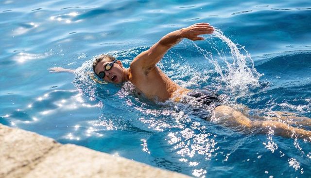 Open water freestyle swimmer cutting through sunlit coastal blue near dock