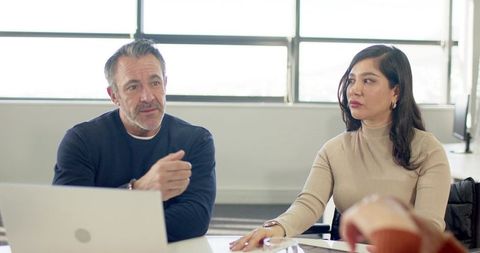 Middle-aged male and female colleagues discussing project strategy in modern office
