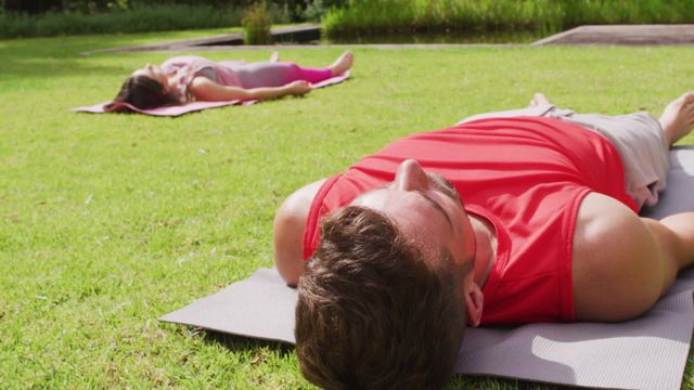 Caucasian man and woman lying on yoga mats with their eyes closed, practicing relaxation techniques in a sunny garden. Ideal for content on fitness, healthy living, outdoor activities, and mindfulness practices. Can be used in articles about yoga benefits, promoting wellness retreats, or advertisements for fitness routines especially suited for couples or outdoor environments.