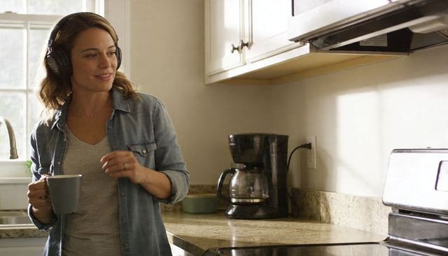 Woman wearing headphones holding coffee mug in cozy morning kitchen, sunlit lifestyle