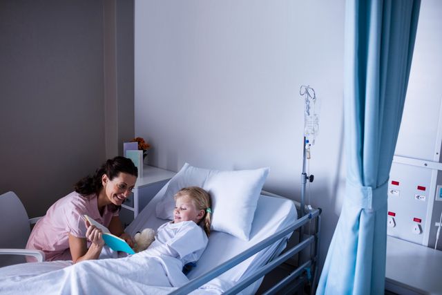 Mother reading a book to her daughter who is lying in a hospital bed. The scene depicts a warm, supportive environment in a healthcare setting. Ideal for use in healthcare promotions, family support materials, and pediatric care advertisements.