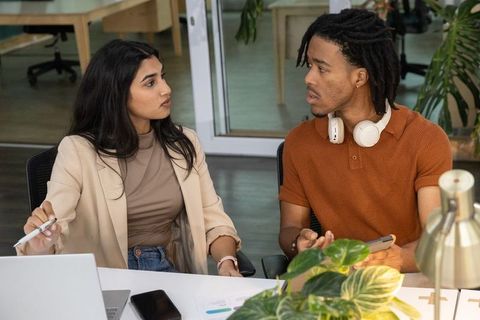 South asian woman and black man collaborating over charts and laptop in modern office team