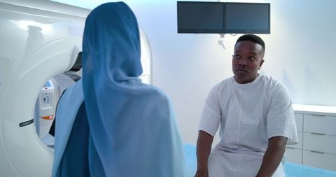 Male patient consulting with radiology technologist beside ct scanner in hospital exam room