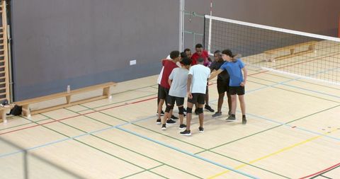 Diverse male volleyball team huddling on indoor court showing teamwork and focus