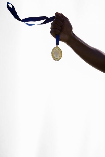 Hand of an athlete holding a gold medal with a blue ribbon against a white background. Ideal for use in sports-related promotions, motivational posters, articles about achievement and success, and advertisements for athletic events or competitions.