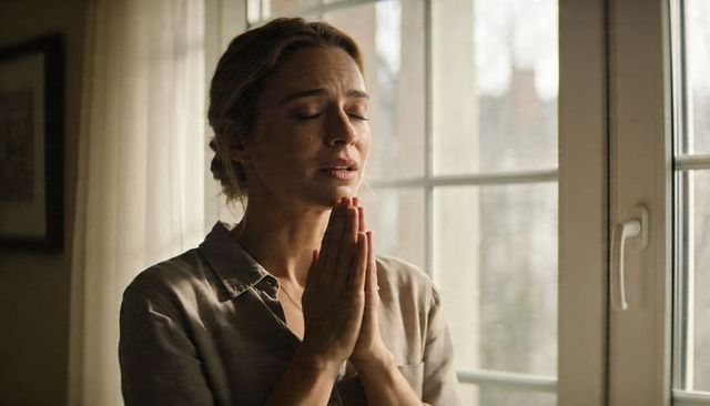 Woman praying by window in soft daylight, contemplative moment of quiet solitude