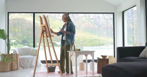 Mature woman painting at easel in bright lakeside studio with panoramic lake view