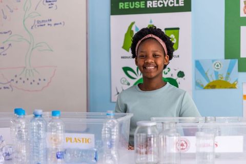 Smiling african american girl sorting plastic recycling in classroom for eco education