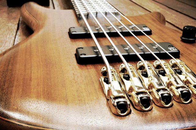 This close-up shows a beautifully crafted wooden bass guitar with golden hardware and strings. Ideal for music-related designs, educational content on musical instruments, and advertisements for music gear. Its detailed shot highlights the craftsmanship, making it suitable for use in articles or blogs discussing guitar design and construction.