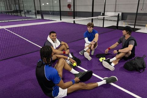 Multiracial teammates sitting on purple court resting after pickleball training