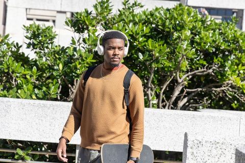 African american student walking on campus holding skateboard and wearing headphones