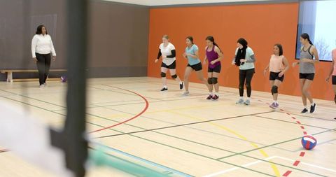 Diverse female volleyball team practicing coordinated warm-up drill on indoor court