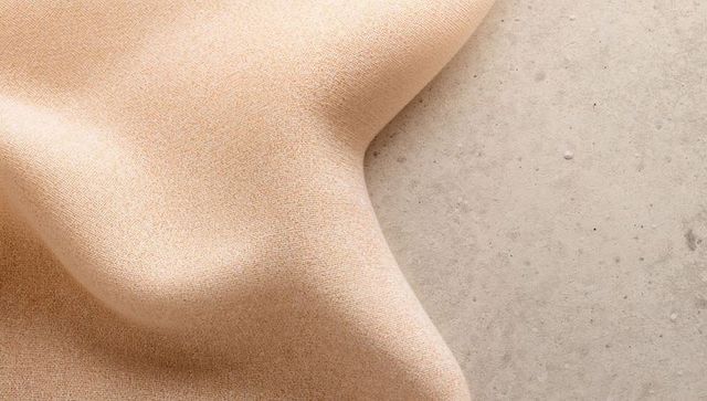 Beige Textured Fabric Draping Over Rounded Form on Concrete Surface with Soft Folds