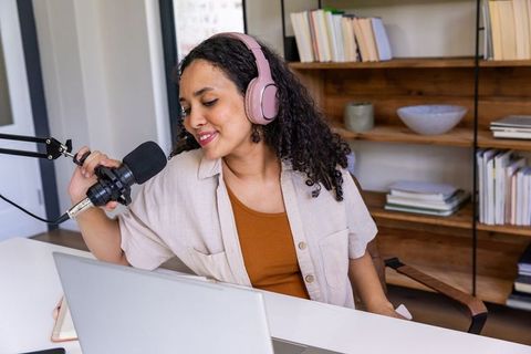 African american woman recording podcast at home desk wearing pink headphones