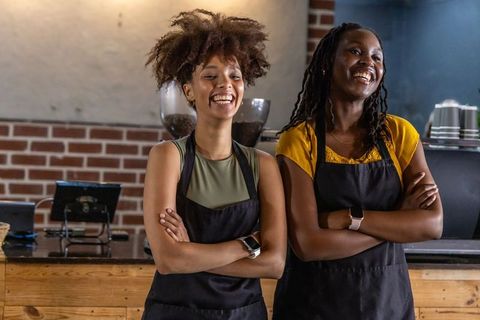 Smiling african american baristas standing behind rustic coffee bar wearing black aprons