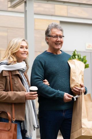 Mature couple enjoying urban stroll arm-in-arm holding coffee and grocery bags