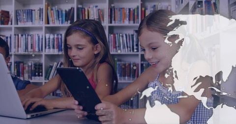 Girls Collaborating Using Tablet and Laptop in Library with World Map Overlay